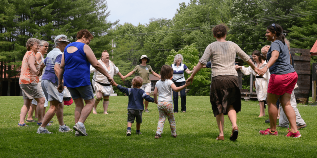 A group of adults and children hold hands together in a circle on a lawn