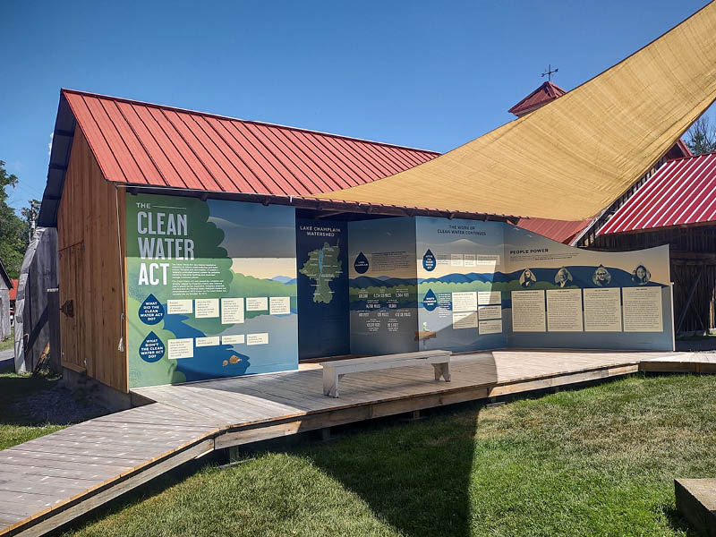 An exhibit with panels wrapped around the front of a building with a red roof on a sunny day.