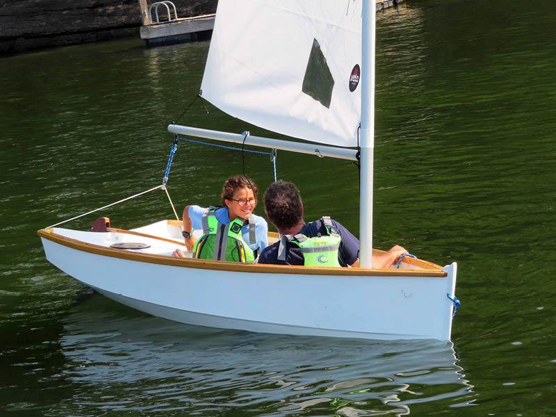 A child and an adult on a small sailing dinghy on calm water