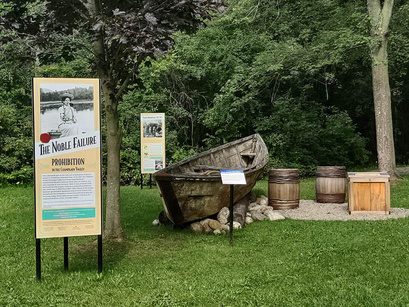 Outdoor exhibit with large text panels and wooden boat with barrels