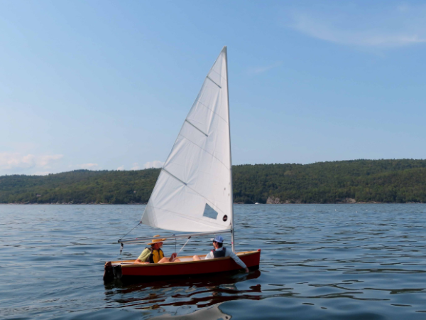 Two adults sit in a small sailing boat as they sail on water